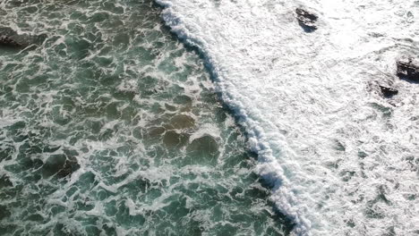 Aerial-drone-shot-of-whitewater-waves-rolling-in-on-a-beach-in-Algarve,-Portugal