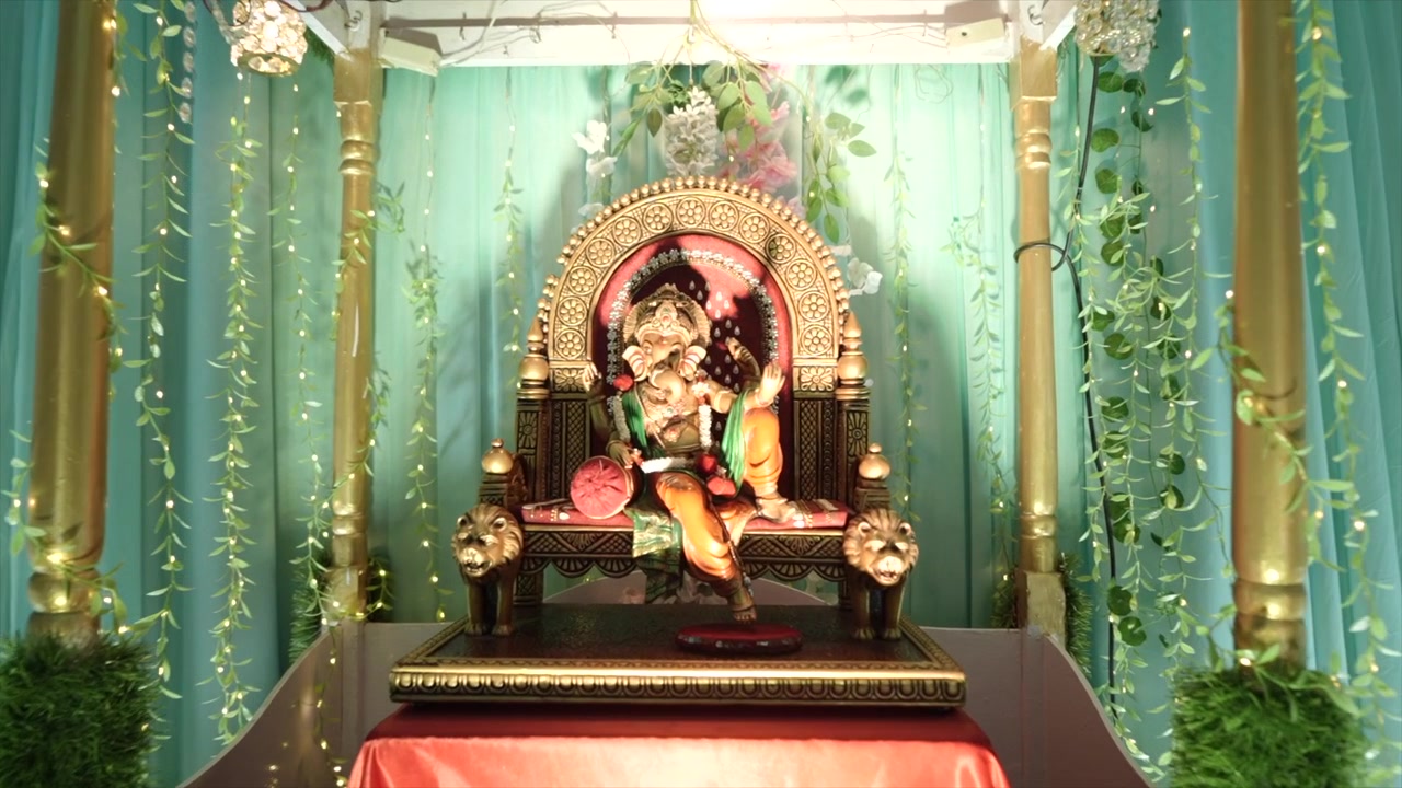 Ângulo dinâmico de uma estátua dourada do Senhor Ganesha repousando sobre um mandap de casamento ornamentado, irradiando bênçãos divinas, prosperidade, elegância e significado espiritual.