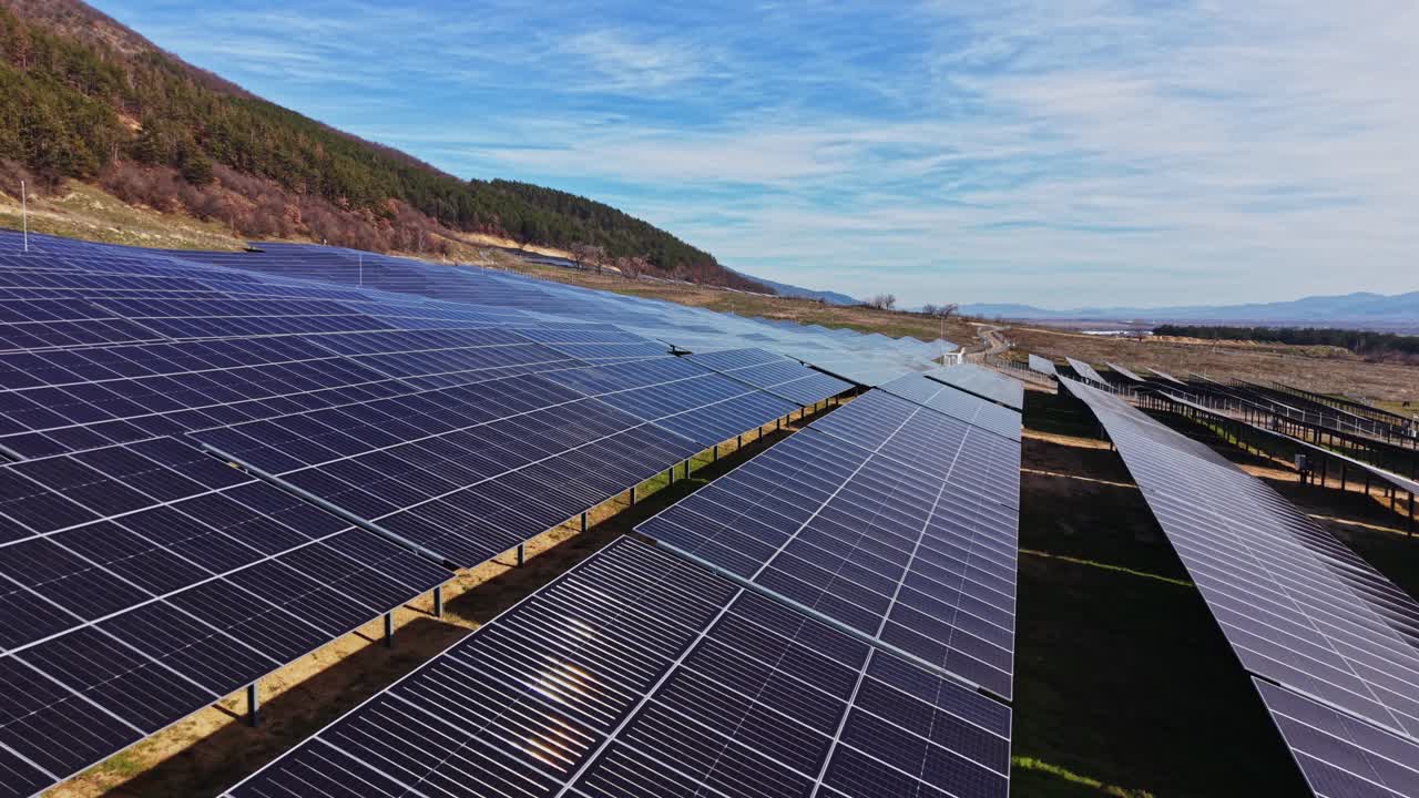 Solpaneler dækker marker under blå himmel med bjerge i baggrunden