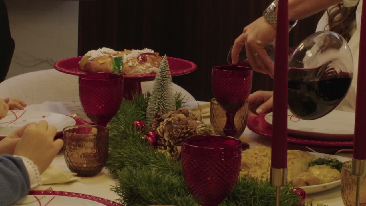 Christmas dinner table with red glasses, bolo rei cake, and wine being poured