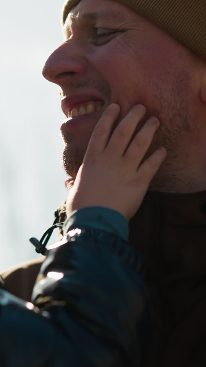 un padre llevando a su hijo, el niño está jugando con su barbilla, con reflejo de luz detrás del niño y poste eléctrico en el fondo