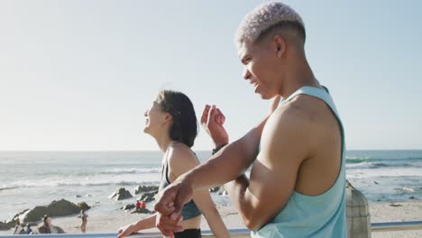 una feliz pareja biracial estirándose en la playa, en cámara lenta