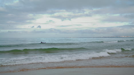 Surfista-Nada-Las-Olas-Del-Océano-En-La-Vista-Vertical-Del-Día-Nublado.-Salpicaduras-De-Agua-De-Mar-Rodante