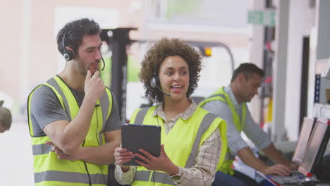 male and female workers wearing headsets in logistics distribution warehouse using digital tablet