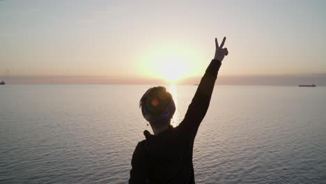 una joven muestra el signo de la victoria en la cima de la colina contra la impresionante vista y el sol