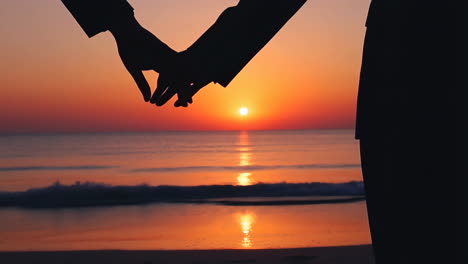 silhouetted couple holding hands at sunset on the beach