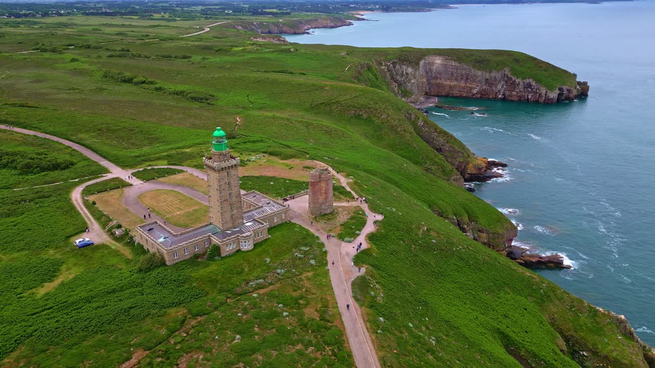 Iconic Cap Fréhel lighthouse and surrounding landscape on green cliffs overlooking sea, Brittany, France. Aerial drone pov