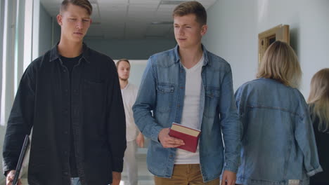 A-group-of-students-walk-along-the-corridor-of-the-university-school-college-communicate-talk-and-smile.-A-large-group-of-people-walking-in-the-hall-of-an-educational-institution-with-books-in-their-hands.