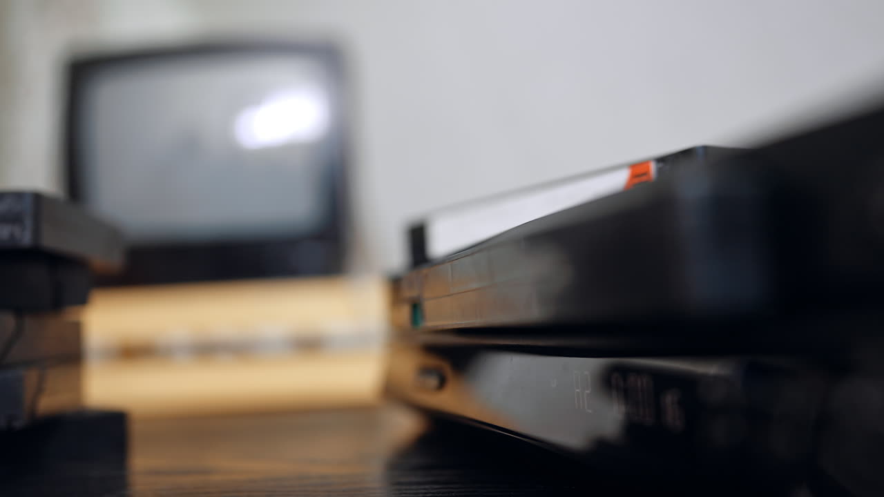 Inserting tape into old video player. A VHS cassette is guided into a vintage video recorder placed near an old TV set