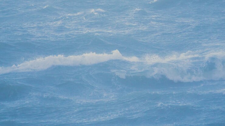 Calm Seagull Flying Over Rough Stormy Choppy Breaking Blue Sea Waves in Slow Motion. Powerful Turbulent Coastline Surf Swell in British Bay During Extreme Weather 4K.