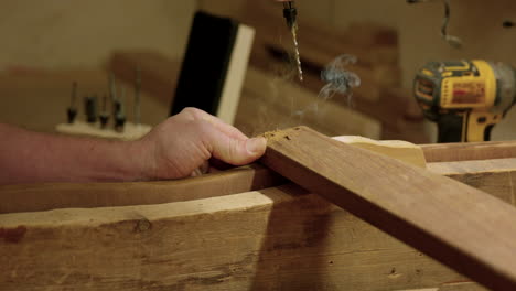 Man-drilling-hole-into-wood-jig---close-up-on-hands-and-drill-bit