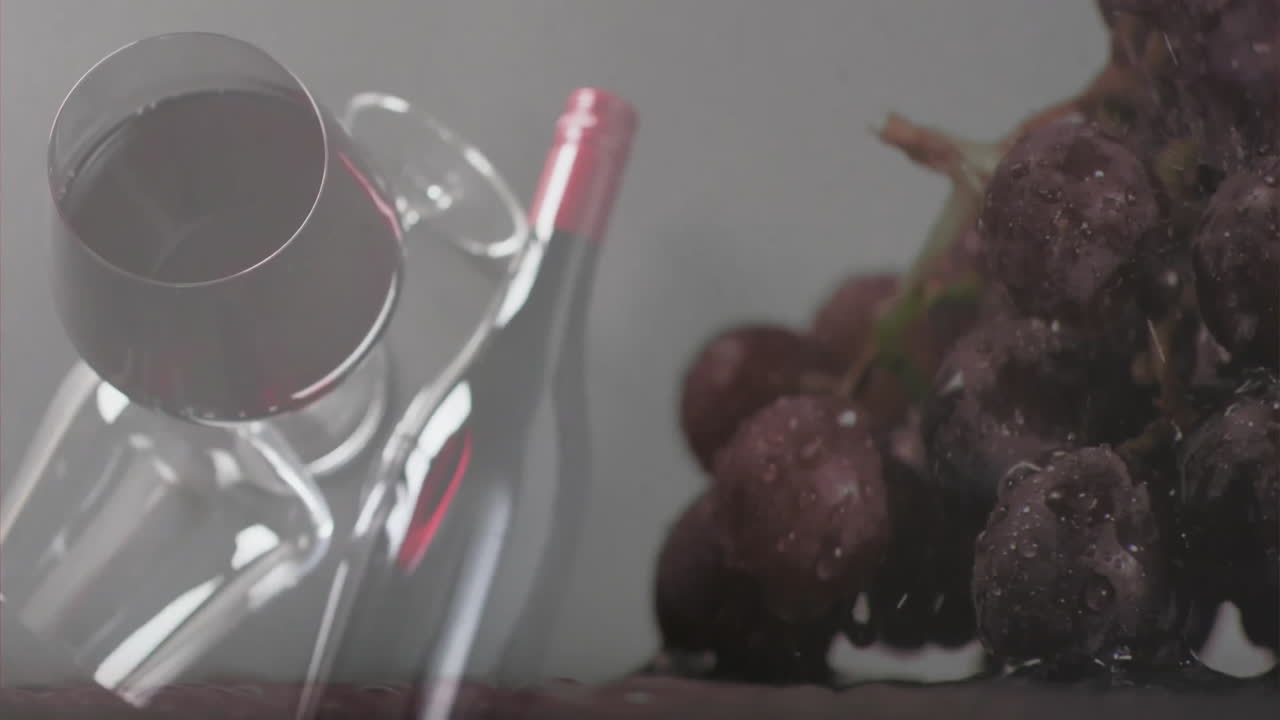 compuesto de vidrio y botella de vino tinto sobre uvas y fondo gris