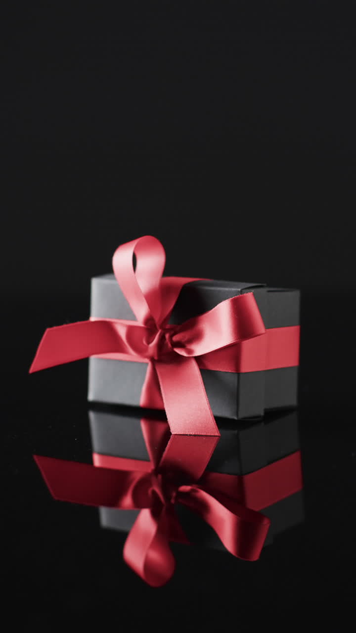 Vertical video of gift box with red ribbon and copy space over black background