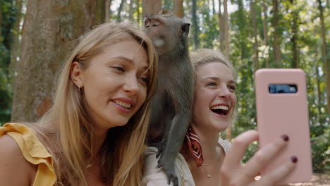 best-friends-using-smartphone-taking-photos-with-monkey-sitting-on-shoulder-two-women-having-fun-posing-with-monkeys-at-wildlife-zoo-tourists-travel-bali