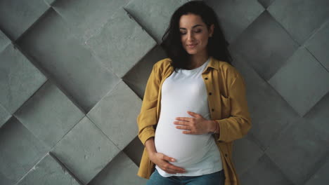 una joven embarazada feliz sonríe sosteniendo y acariciando su vientre