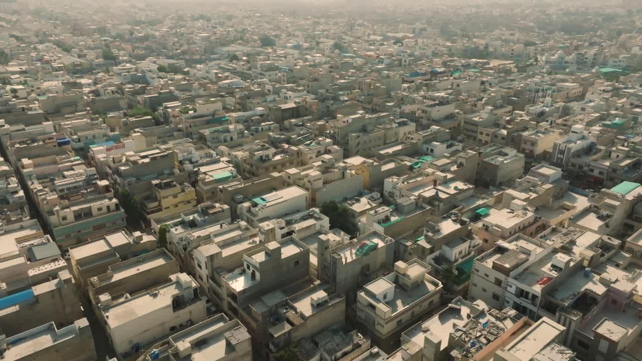 Toma aérea de dron moviéndose hacia atrás sobre la congestionada ciudad de Ancholi con hileras de edificios en la zona residencial de Karachi, Pakistán, en un día soleado y brillante