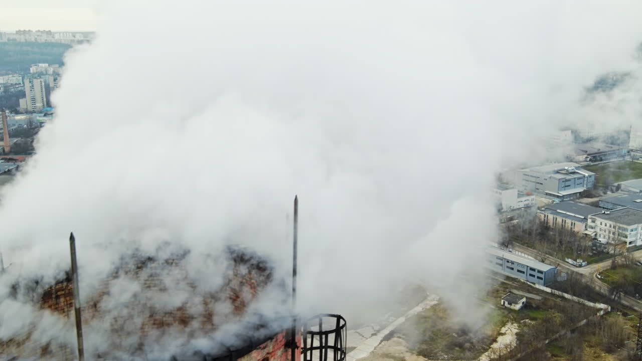 Aerial drone view of thermal station with smoke coming out of the tube. Buildings, roads and bare trees on the background. Cloudy weather. Chisinau, Moldova