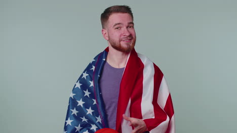 un joven barbudo fanático del baloncesto sosteniendo la bandera de los estados unidos haciendo el gesto del ganador, bailando solo