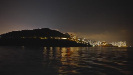 Aufnahme-Von-Einem-Boot-Aus,-Das-Mitten-In-Der-Nacht-Links-Von-Einer-Urbanisierten-Insel-Fährt-4