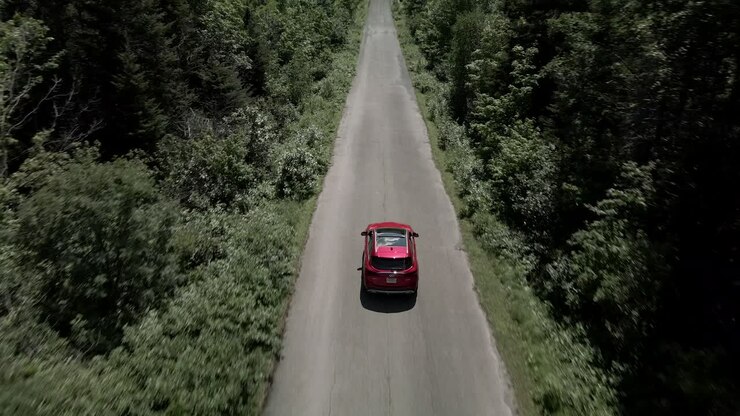 Un'auto di lusso Infiniti rossa con tettuccio apribile oscurato che guida su una strada lunga e tortuosa attraverso gli alberi verdi in Canada in una giornata di sole - drone aereo, ripresa ascendente