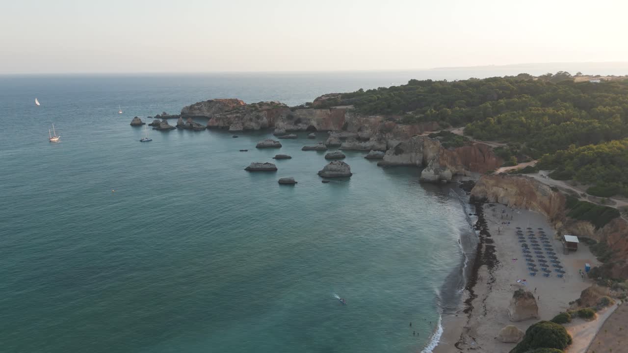 Aerial view of sailboats navigating the turquoise waters near the cliffs and beach of Alvor, in the Algarve region, Southern Portugal