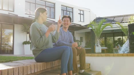 Video-of-happy-diverse-couple-talking-and-drinking-coffee-in-garden