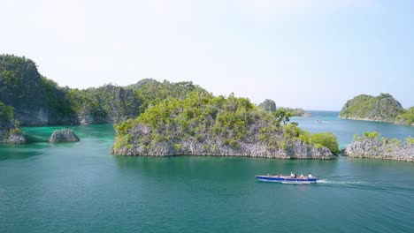 Piaynemo-bay-with-small-trimaran-motorboat-with-passengers-onboard-at-Raja-Ampat-Indonesia,-Aerial-approach-shot