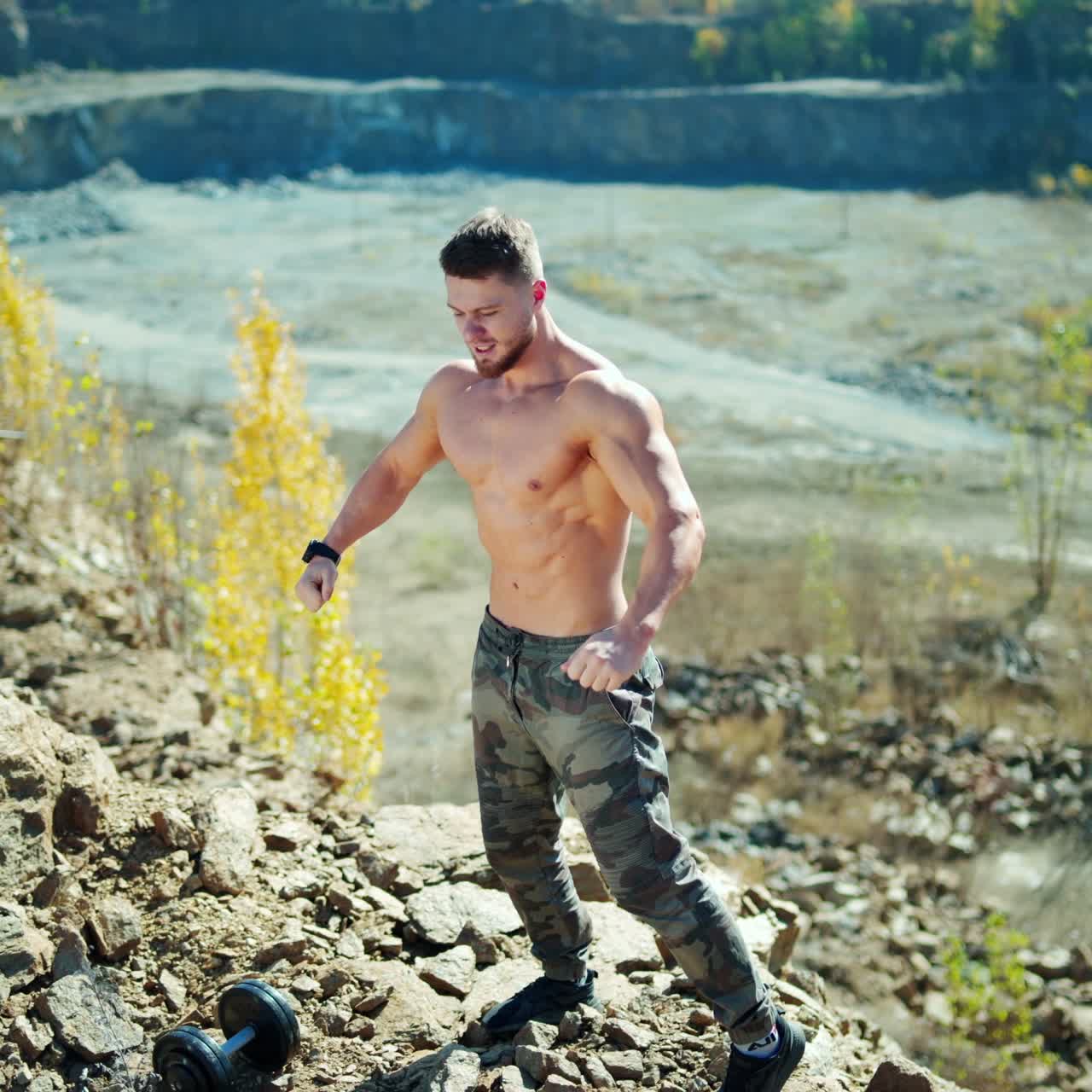 Portrait of shirtless man outdoors. Handsome sporty athlete posing in front of a camera and showing his defined muscles on rocky background.