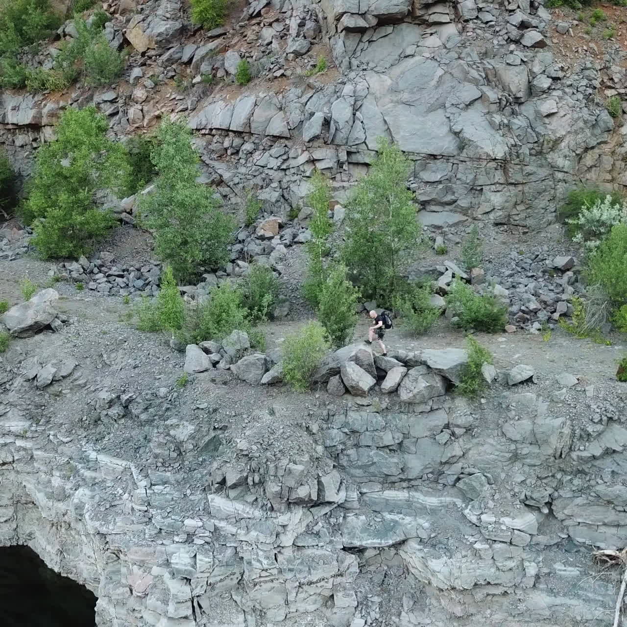 Top view of an active tourist walking on the canyon with stone surface in summer. Male traveller hiking in the mountains near the lake outside.
