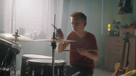 teen drummer rehearsing in sunlit room teenager in red t shirt playing drums during rehearsal in light room in daytime at home