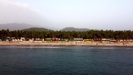 drone volando hacia la orilla de una playa en una playa tropical soleada con turistas, india, goa, palolem