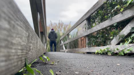 Man-Walks-On-Footbridge-With-Wooden-Handrails