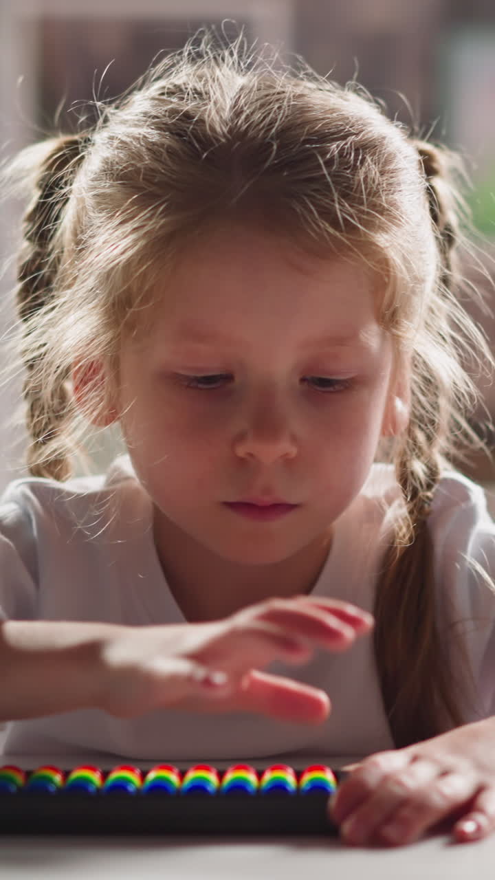 Serious little schoolgirl with blonde thin braids learns to do sums with abacus at home mental arithmetic lesson close view slow motion