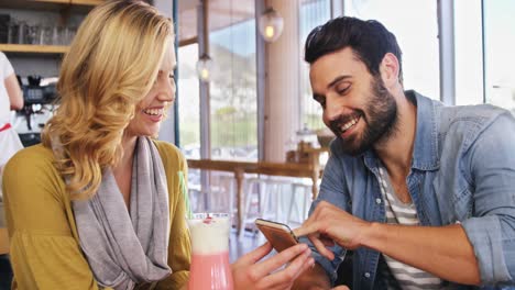 couple using mobile phone while having a cup of coffee and milkshake