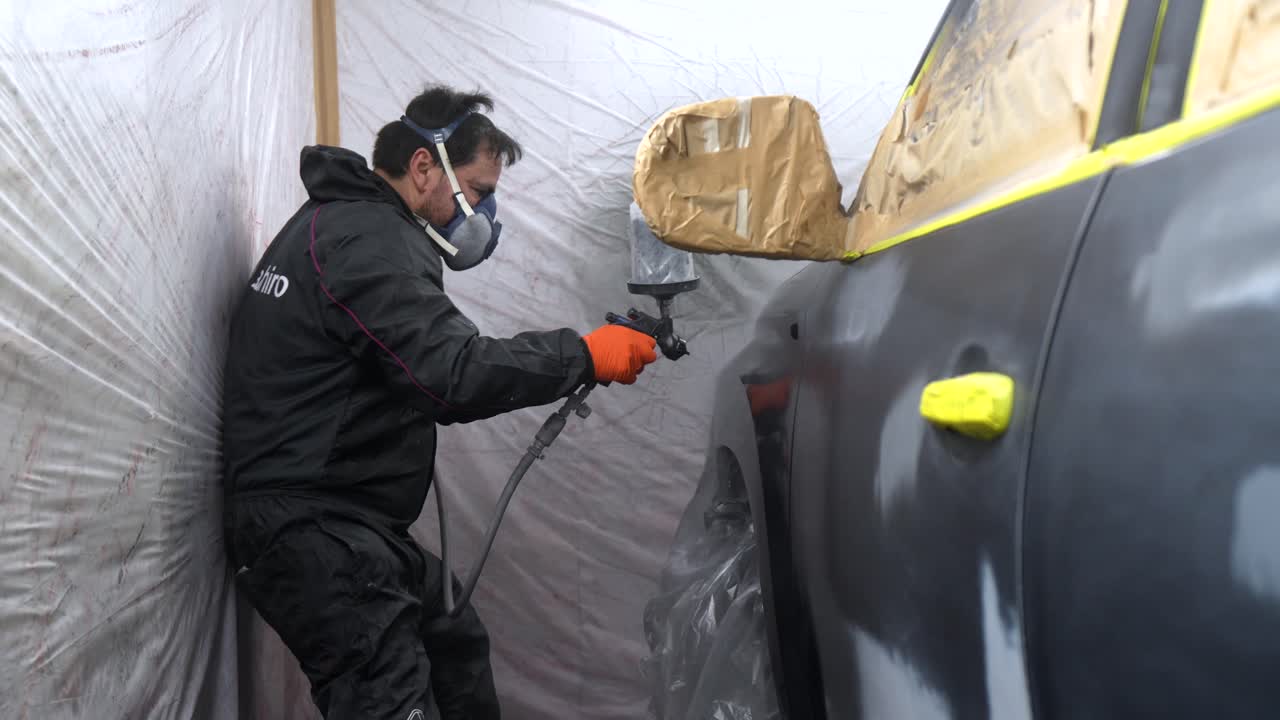 Man in Protective Gear Spray Painting a Car in a Workshop