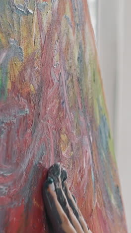 talented woman artist at work on colorful abstract painting making strokes by palm on canvas in studio slow motion extreme close side view