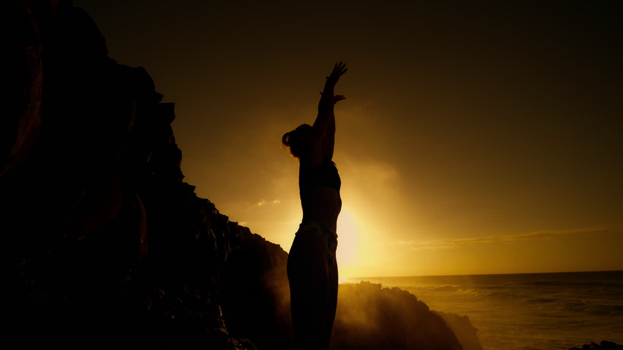 Woman practicing yoga at sunrise/sunset on a rocky coast