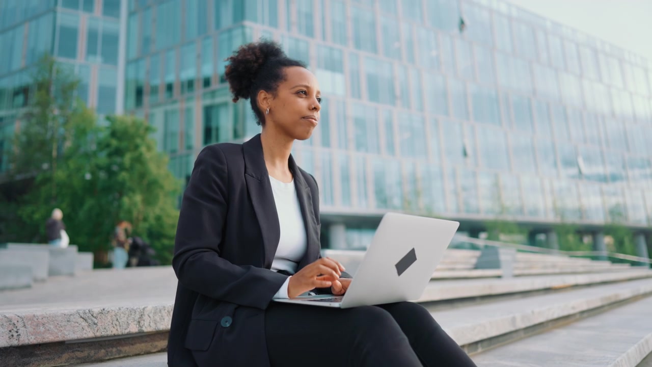 Professional Woman Working on Laptop Outside Modern Office Building