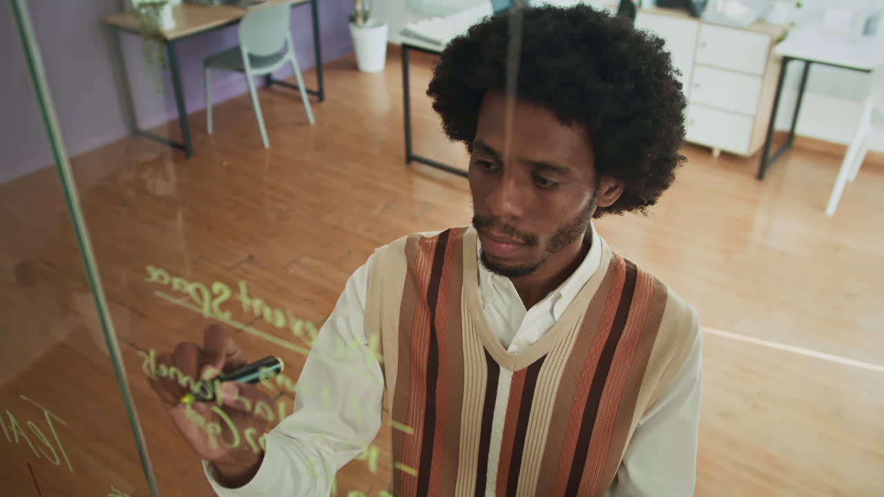 Analista afro-americano criando esquema em parede de vidro e usando tablet