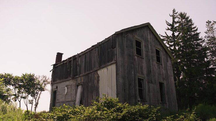Profile backlit view of abandoned wooden cabin broken windows, grey wood