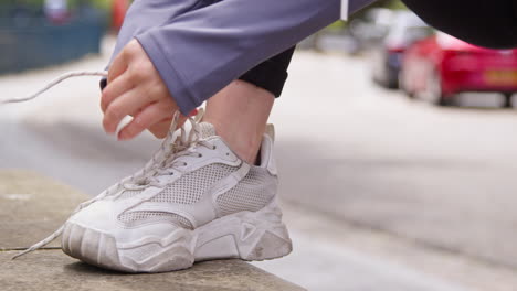 Close-Up-Of-Woman-Tying-Laces-On-Training-Shoe-Before-Exercising-Running-Along-Urban-Street