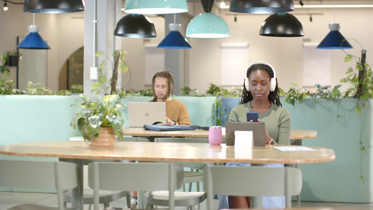 African American coworkers starting work at table, woman using phone and tablet, man typing laptop