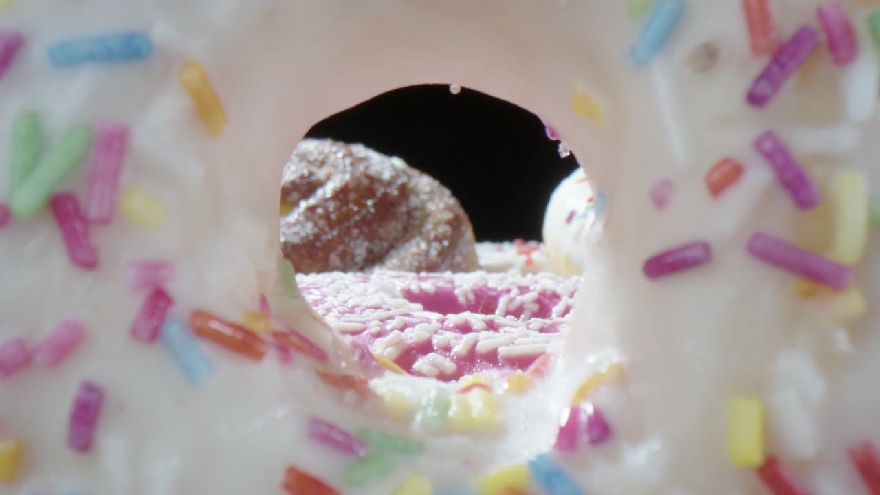 Obiettivo sonda attraverso il foro di una ciambella glassata con zuccherini colorati, fresca di panificio
