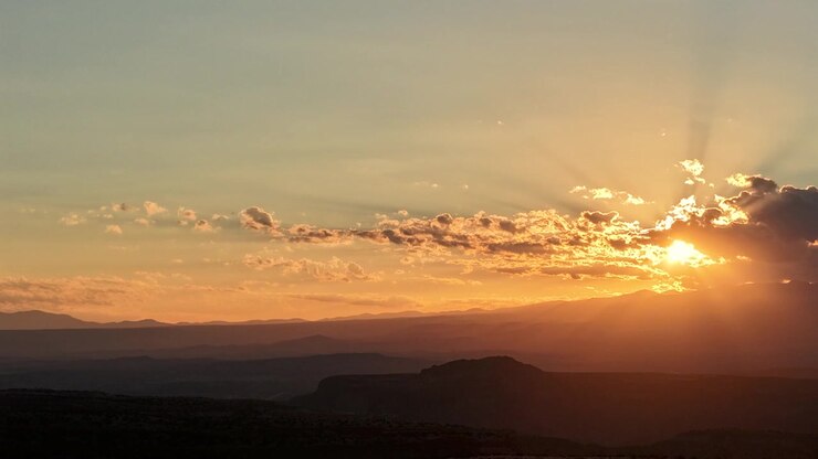 Timelapse 4K con dron paneando desde un radiante amanecer dorado que irrumpe entre las nubes matutinas. La vista panorámica revela montañas silueteadas y profundos cañones de desierto alto a lo largo del paisaje del Suroeste.