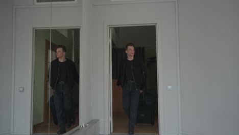 high school student walking out of room carrying travel bag leaving door open behind with large vertical mirror on wall reflecting scene interior corridor