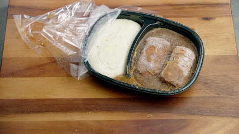 contenedor de comida congelada procesada de plástico que se cae sobre la mesa de comedor con cristales de hielo rompiéndose