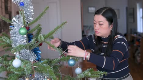 アジア人女性がクリスマスツリーの装飾品を 取り下ろしています