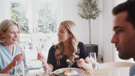 Family-With-Senior-Parents-And-Adult-Offspring-Make-A-Toast-Before-Eating-Meal-Around-Table-At-Home