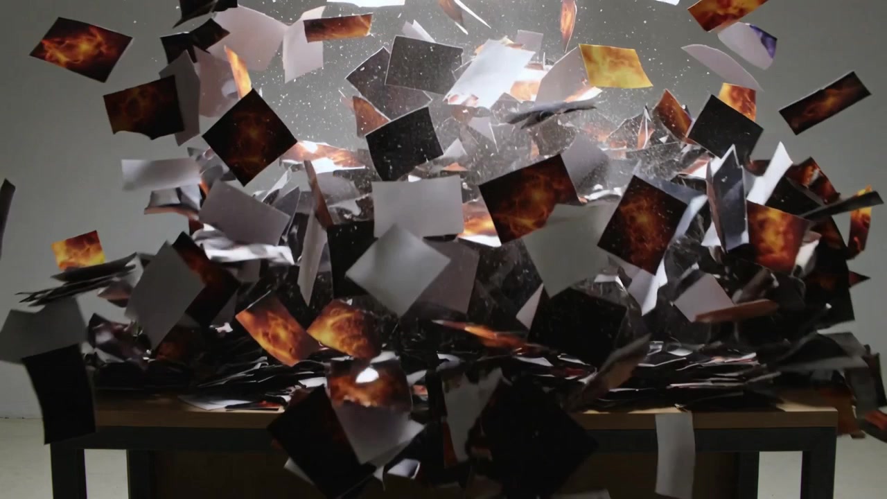 Shifting top layers causing printed paper pile erupting over wooden table, scattering orange prints