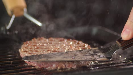 man's hand with a spatula presses on fried burger in pan.